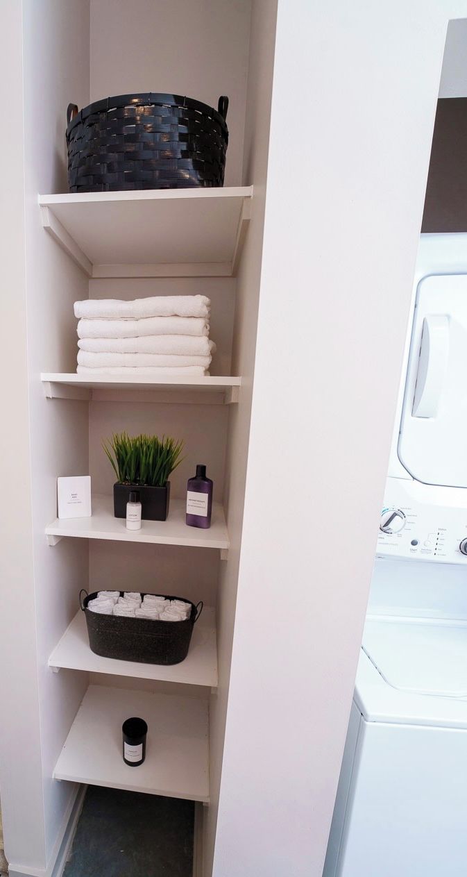 A laundry area with shelves holding towels, a basket, and a potted plant.