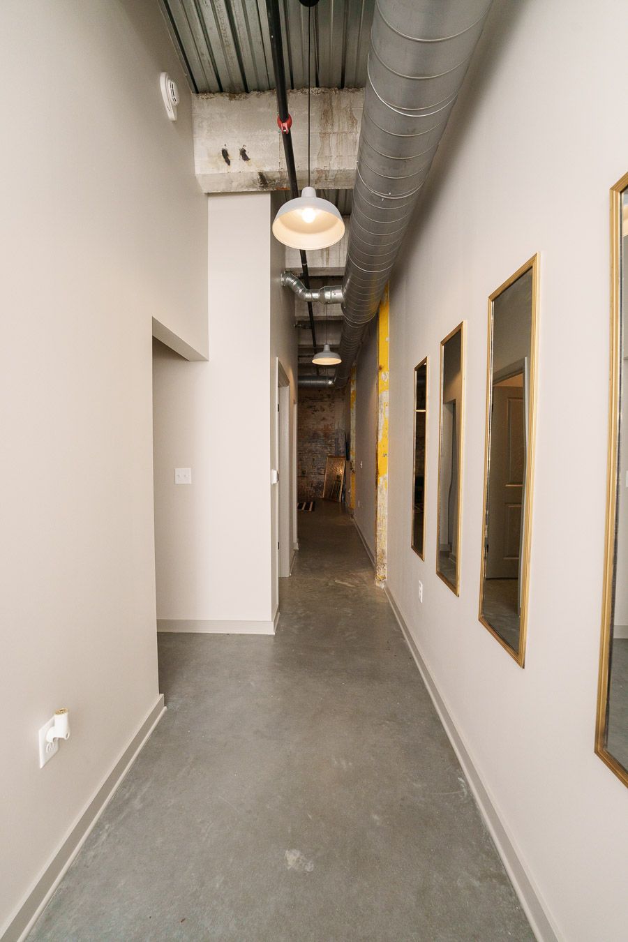 A hallway with a concrete floor, a ceiling with exposed ductwork, and a hanging light fixture.