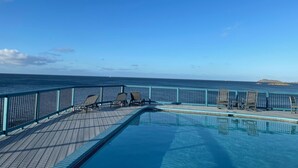 Et poolområde med havudsigt, træterrasse og liggestole.