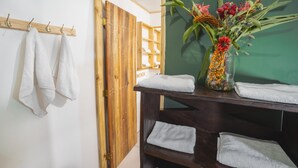 A bathroom with white towels on a rack, a wooden door, and a vase with flowers on a shelf. - Veragua Rainforest Lodge (Río Blanco)