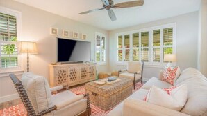 A living room with a television, a ceiling fan, and a large window with blinds. - Princeville Paradise - Luxury A/C (Princeville)