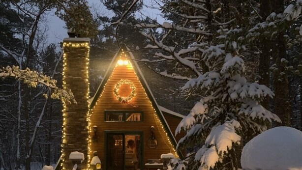 Een gezellig huisje met een warme gloed, omgeven door met sneeuw bedekte bomen.