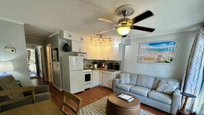 Un espacio habitable compacto con kitchenette, una zona de comedor con mesa y sillas, un sofá y un ventilador de techo.