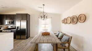 A modern kitchen with dark cabinets, stainless appliances, and a wooden dining table with a bench.