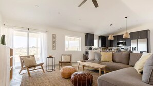 A spacious living area with a sofa, chairs, a coffee table, and a kitchen in the background.