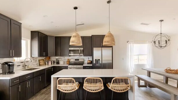 A modern kitchen with dark cabinets, a large island with bar stools, and pendant lighting.