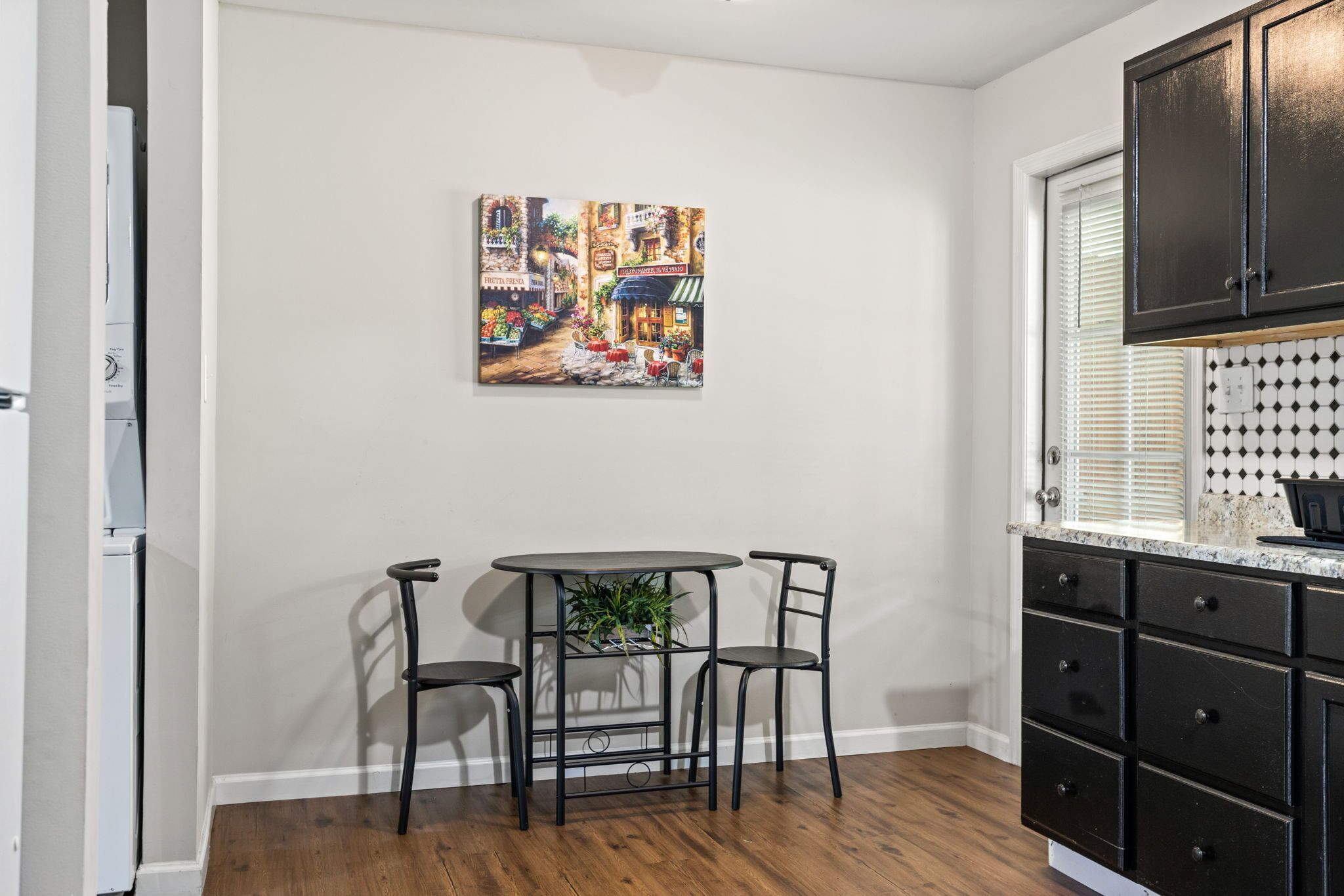 Une cuisine avec une table à manger, des chaises et un tableau accroché au mur.