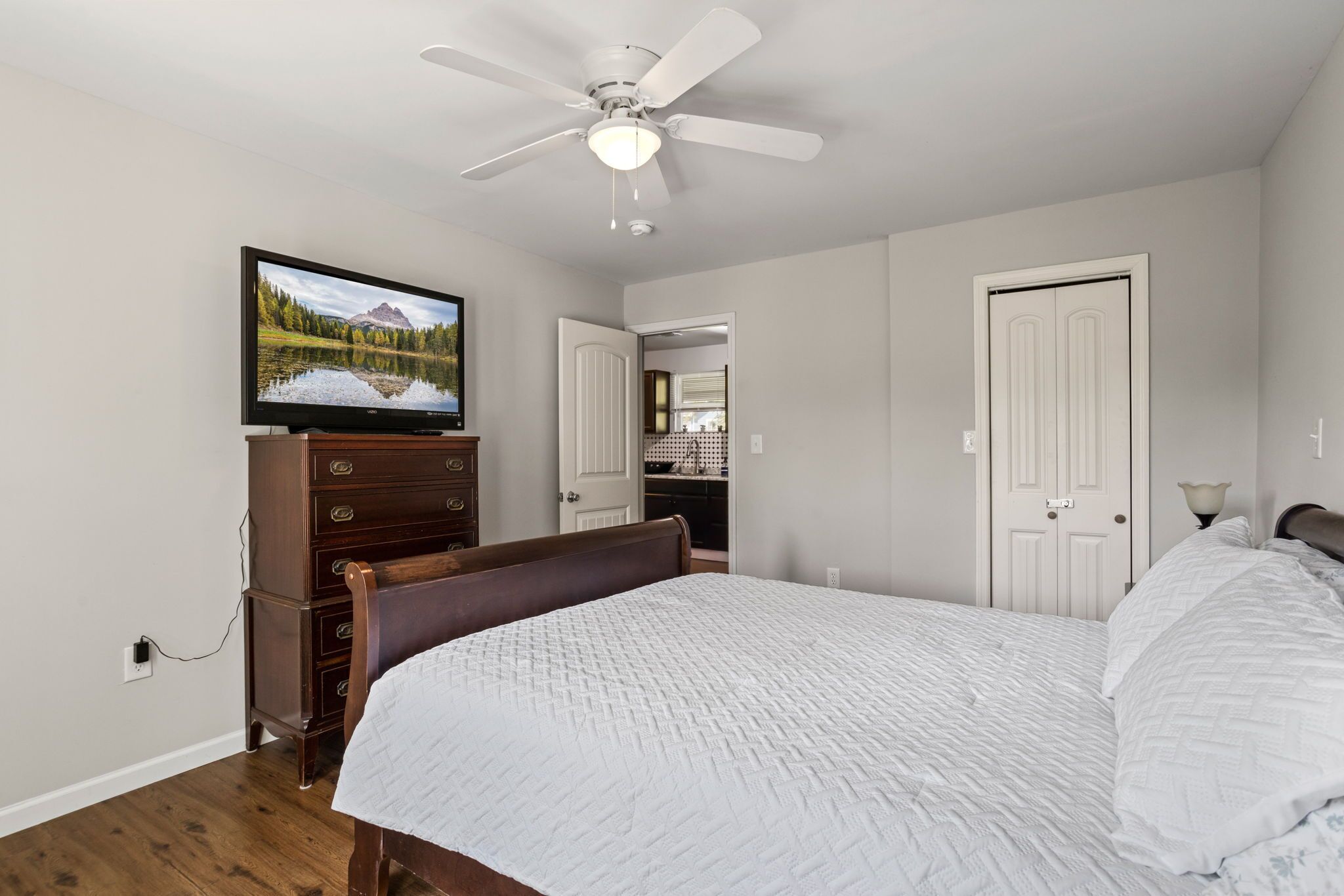 A bedroom with a bed, dresser, television, ceiling fan, and white doors.