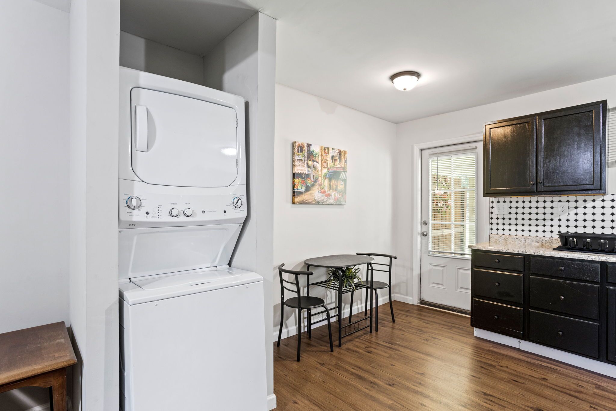 Une cuisine compacte dotée d’un lave-linge et d’un sèche-linge intégrés, d’un coin repas avec une petite table et des chaises, et de meubles de couleur noire.
