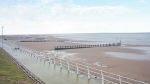 Ein Strand mit einer Betonpromenade und einem Holzzaun.