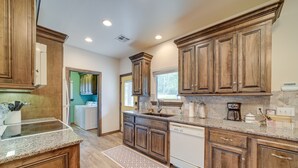 A kitchen with wooden cabinets, granite countertops, a dishwasher, and a coffee maker. - Cozy Checotah Retreat w/ Deck Near Eufaula Lake (Checotah)