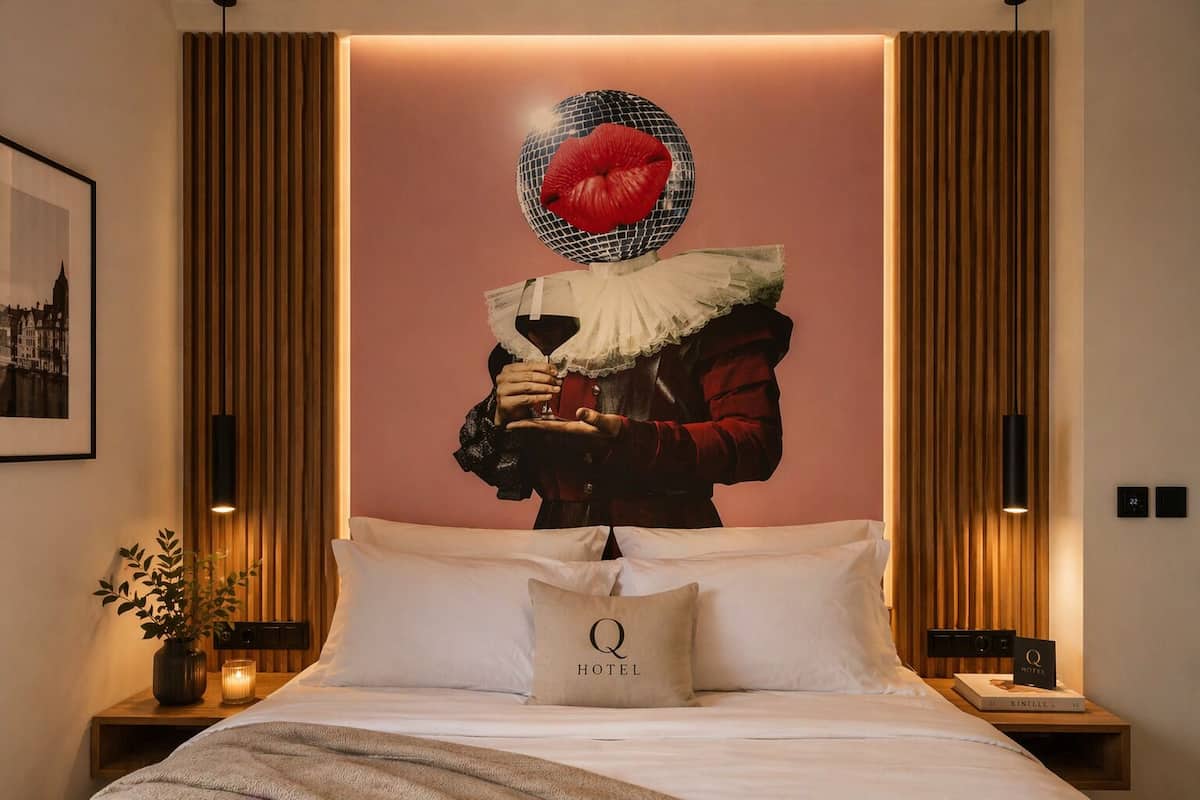 A hotel room with a large bed, a framed picture on the wall, a decorative wall piece, and a bedside table with a book and a candle.