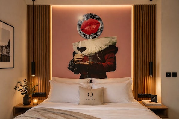 Habitación de hotel con una cama grande, un cuadro enmarcado en la pared, un adorno decorativo y una mesita de noche con un libro y una vela.