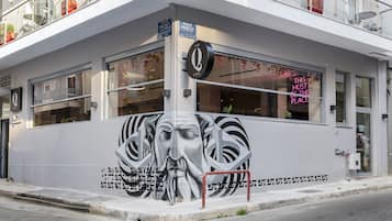 A building with a large mural on the side, a cafe sign, and a neon sign.