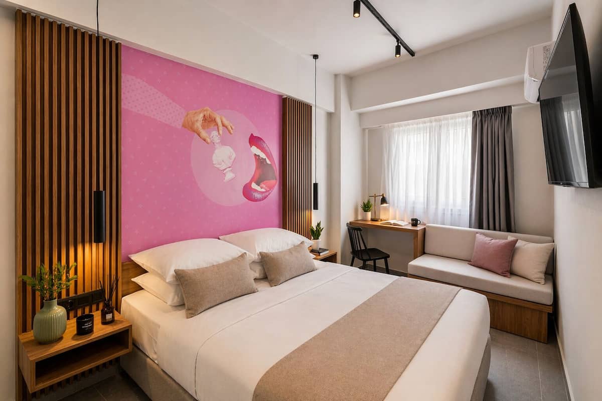 A modern hotel room with a large bed, a desk, a sofa, and a wall mural.