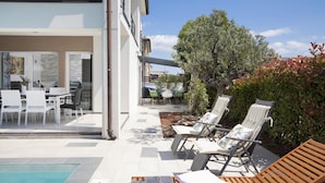 A modern outdoor pool area with lounge chairs, a dining table, and a view of the building's exterior.