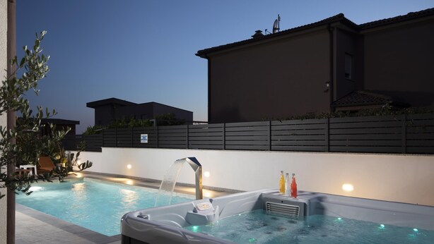 An outdoor swimming pool with a hot tub, surrounded by a low wall and a building.