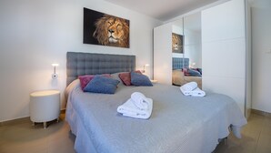 A modern bedroom with a large bed, a headboard, a nightstand, a wall-mounted mirror, and a framed picture of a lion.