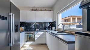 A modern kitchen with white cabinets, a black marble countertop, and a view of a building through a window.