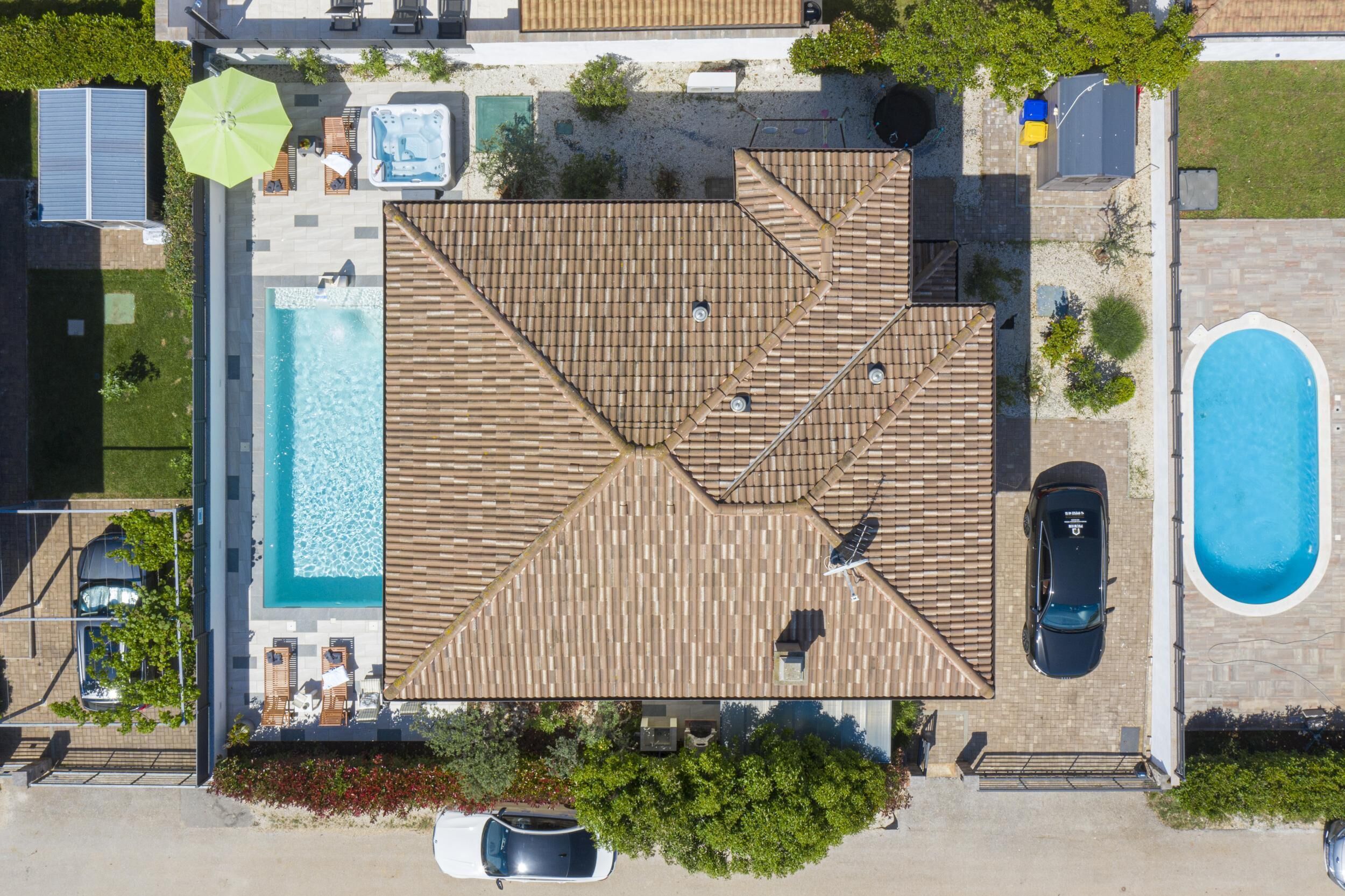 Luchtbeeld van een woonhuis met zwembad, overdekt terras en auto op de oprit.
