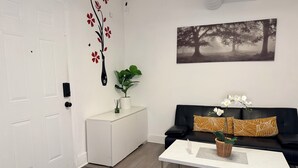 A modern living room with a white sofa, a coffee table, and a painting of trees. - Modern Private Share Bedroom Bus stop to NYC (Englewood)