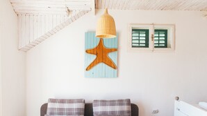 Een gezellige kamer met een houten plafond, een grijze bank met geruite kussens, een klein tafeltje met een blauwe placemat en een houten sterdecoratie aan de muur.