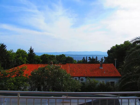 A building with a red-tiled roof, surrounded by greenery and trees, with a clear sky and distant mountains. - Barba Zoran 2 (Bol)