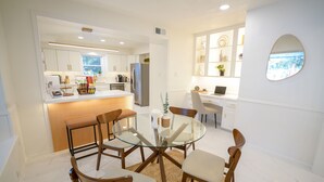 Una cocina moderna con armarios blancos, un refrigerador empotrado y una zona de comedor con mesa de vidrio y sillas de madera.