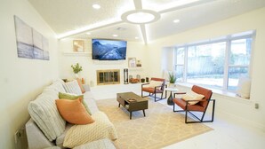 Amplia sala de estar con chimenea, asientos cómodos y ventanas grandes que ofrecen vistas al exterior.