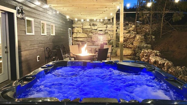 Un bain à remous avec un mur en pierre en arrière-plan, entouré de meubles d’extérieur, situé sous une terrasse en bois.