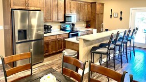 Une cuisine moderne avec des meubles en bois, un réfrigérateur en acier inoxydable et un coin bar doté de tabourets hauts.