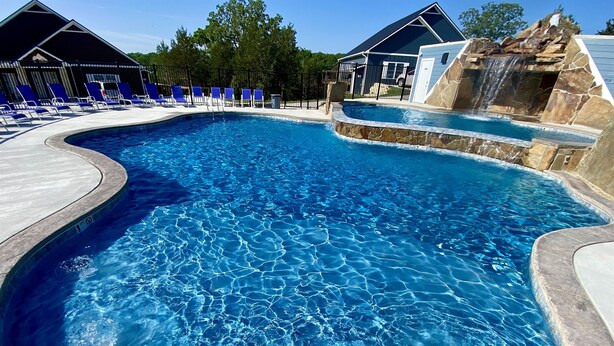 A swimming pool with clear blue water, surrounded by lounge chairs and a stone waterfall feature. - YES! 🎸FamilyPlace 🏊‍♀️POOL/WaterFall💦HOTTUB 🔥FIREPIT🎱POOLTABLE⚡EV🎡FUN❤️LUV (Branson)
