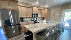 A modern kitchen with wooden cabinets, stainless steel appliances, a granite countertop, and a bar area with stools. - ELITE📍nearSIGHTnSOUND 🏊‍♀️POOL/WaterFall💦HOTTUB ⚡EV 🔥FIREPIT 🎱POOLTABLE 🎡 (Branson)