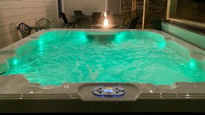 A hot tub with a control panel, surrounded by outdoor seating and string lights. - ELITE📍nearSIGHTnSOUND 🏊‍♀️POOL/WaterFall💦HOTTUB ⚡EV 🔥FIREPIT 🎱POOLTABLE 🎡 (Branson)