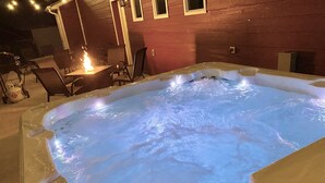 Un bain à remous doté d’un foyer, entouré de mobilier d’extérieur et d’un mur en bois.