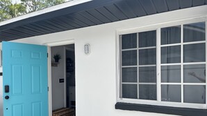 A white building with a turquoise door, a large window, and a black awning.