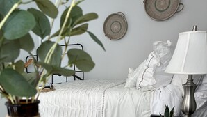A neatly arranged bedroom with a bed, bedside table, lamp, and decorative wall hangings.