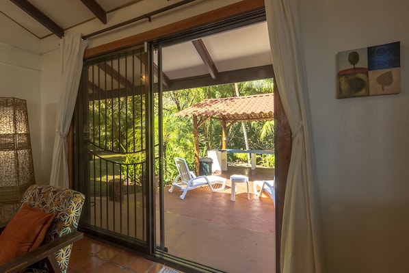 A room with a sliding glass door leading to an outdoor patio with a table and chairs, surrounded by lush greenery.