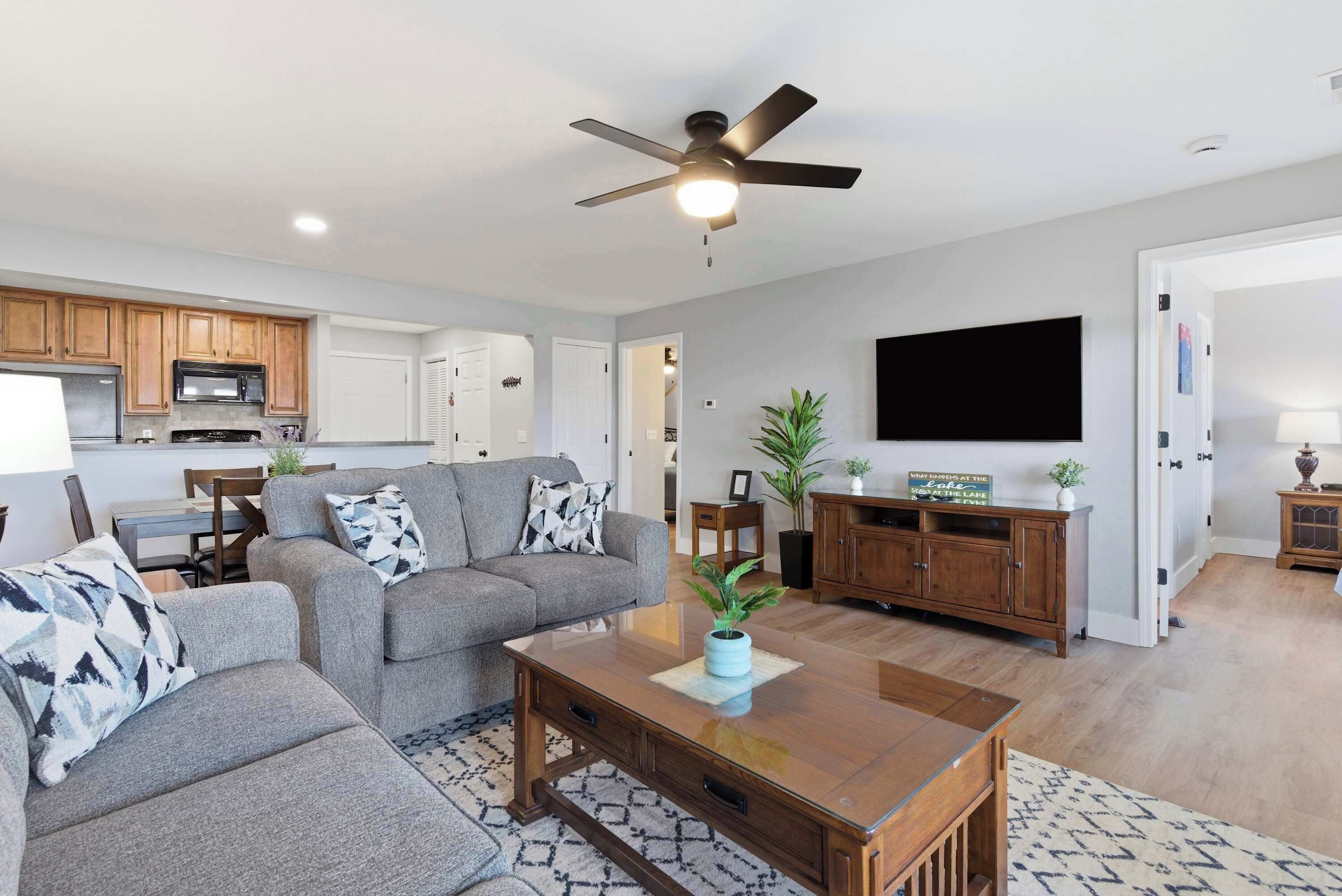 A modern living room with a sofa, coffee table, and TV. There is a kitchen area with cabinets and a microwave.