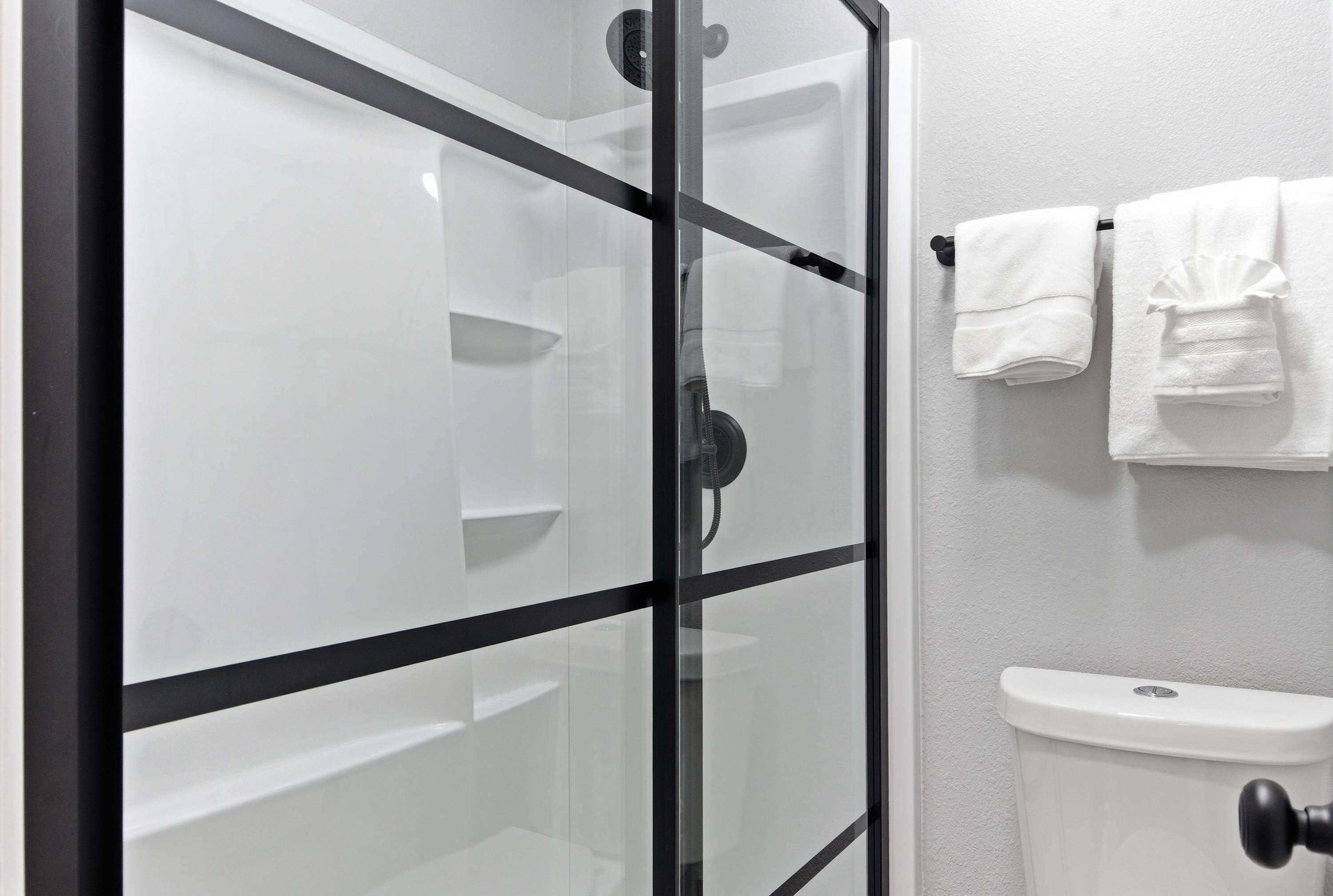 Un baño moderno con cabina de ducha de vidrio, inodoro y toallas ordenadas.