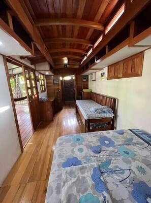 A narrow corridor with wooden flooring and walls, leading to a room with a bed and a bench. - Fun Family Pool Cabin (Pavones)