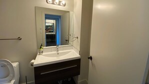 A bathroom with a white sink, a mirror with lights, a blue door, and a toilet.