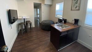 A compact kitchen with a built-in dishwasher, a sink, and a coffee maker. There is a small dining area with stools and a table.
