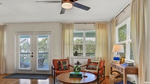 A spacious living room with a wooden floor, a round coffee table, two sofas with cushions, a side table with a lamp, and a ceiling fan.