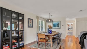 A dining area with a wooden table, chairs, and a glass cabinet with books and games.