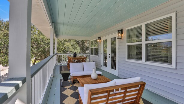 A covered porch with a wooden bench, a table, and a chair.