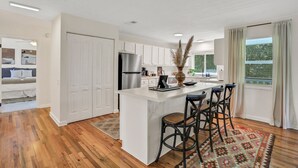 A modern kitchen with white cabinetry, a central island with bar stools, and a view of the outdoors through large windows.