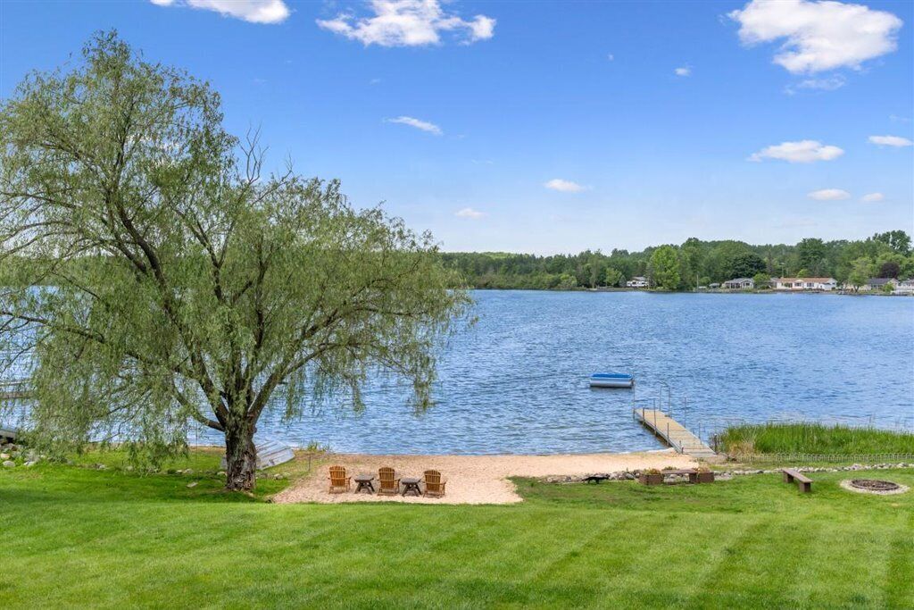 A lakeside property with a dock, outdoor seating, and a large tree.