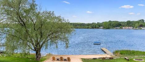 A lakeside property with a dock, outdoor seating, and a large tree.