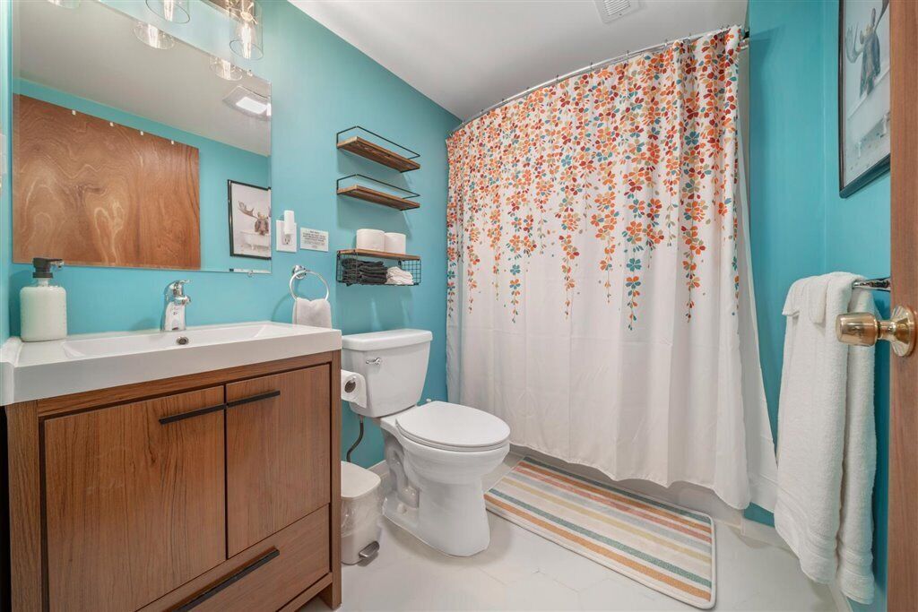 Ein Badezimmer mit Toilette, Holzwaschtisch, Spiegel und einer Duschkabine mit Blumenmuster.